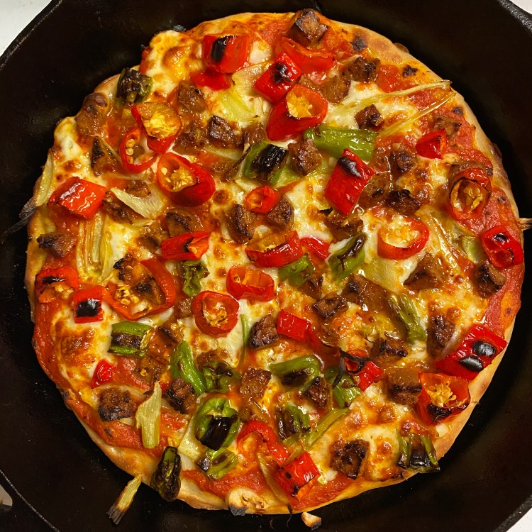 an uncut pizza in a black cast iron pan with the toppings listed in the caption plus lots of cheese