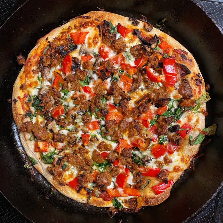 an uncut pizza in a black cast iron pan with the toppings listed in the caption plus lots of cheese