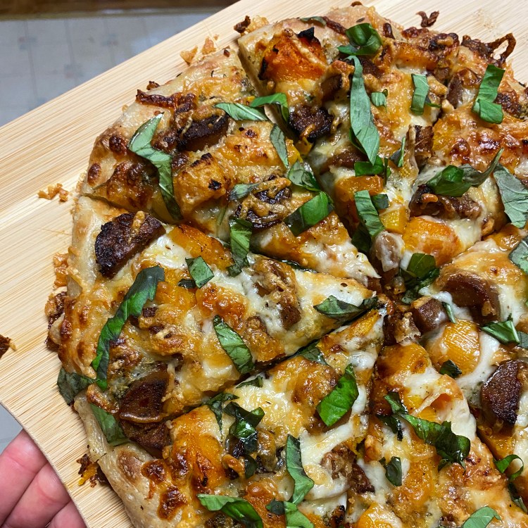 a cut pizza on a wood board with the toppings listed in the caption plus lots of cheese