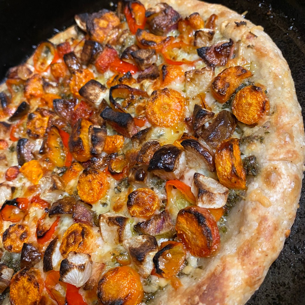 an uncut pizza in a black cast iron pan with the toppings listed in the caption