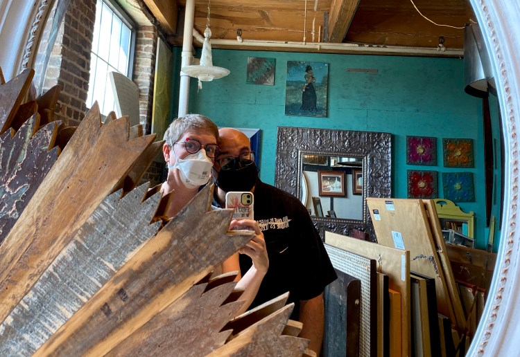 Lee and Pete, both wearing masks, in a store with a turquoise wall and a bunch of framed, reflected in a mirror