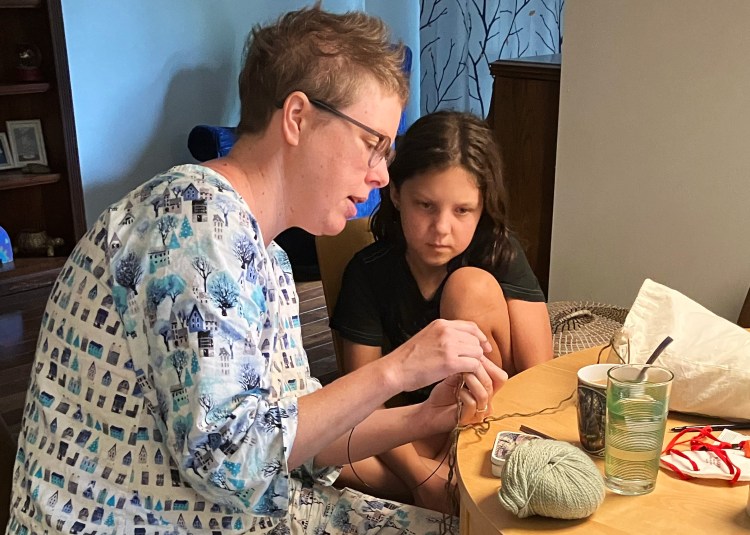 Lee teaching Nico how to knit at a kitchen table