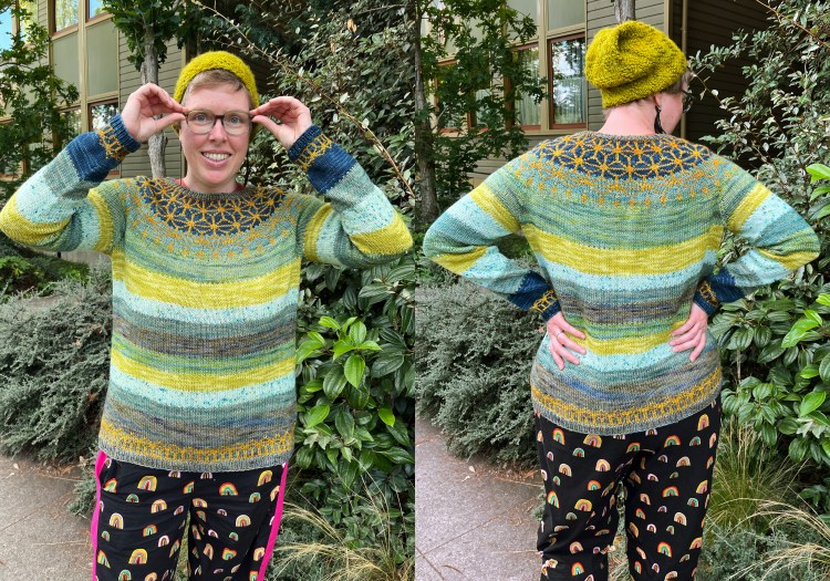 2 photos of Lee standing outside with plants behind, wearing a striped blue and green sweater with a gold colorwork design on the top and bottom edges, black pants with rainbows on them, and a green hat, 1 looking forward and arms up and 1 with back to camera