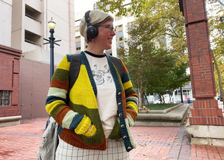 Lee smiling wearing cardigan outside, hands in pockets
