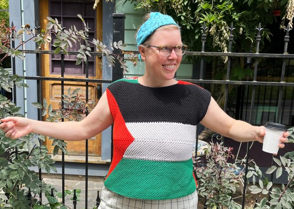 Lee smiling wearing a Palestinian knit flag as a top, arms out