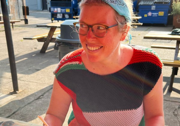 Lee smiling wearing a Palestinian knit flag as a top, showing the shoulder wedges