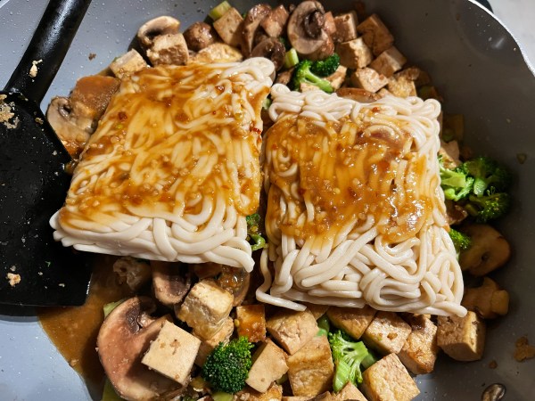 noodles still in their vacuum packed rectangular forms, with sauce on top, in a skillet over tofu, broccoli, and mushrooms