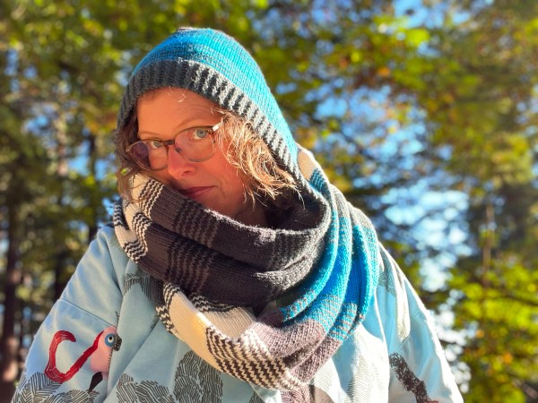 Lee wearing a worsted weight hood with cowl double-wrapped in blue, grey, white shades with wide stripes and 1x1 stripe segments blending between