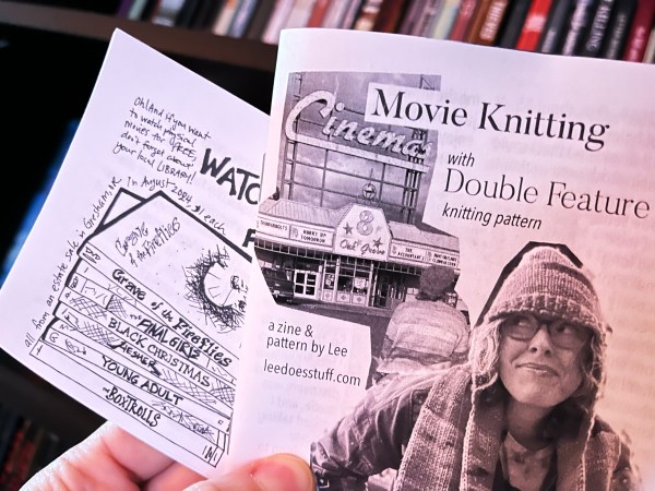 close-up of two zines, the back one with a drawing of a stack of dvds, and the front the cover of Movie Knitting zine, subhead "with Double Feature knitting pattern" and "a zine & pattern by Lee leedoesstuff.com"