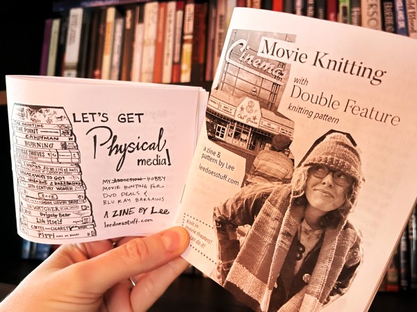 close-up of two zines, the back one "Let's Get Physical Media!" with subtitle "My [addiction, crossed out] hobby movie hunting for dvd deals & blu ray bargains. a zine by Lee leedoesstuff.com and a drawing of a stack of dvds, and the front the cover of Movie Knitting zine, subhead "with Double Feature knitting pattern" and "a zine & pattern by Lee leedoesstuff.com"
