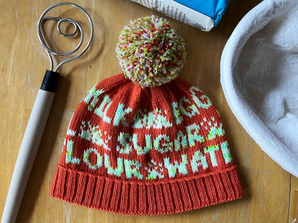 hat with words on it laying flat amongst related items (dough mixer, banneton)—visible words are MILK, EGG, SUGAR, FLOUR, WATER