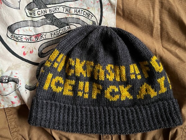 hat with words on it laying flat on top of a jacket with patches—visible words are FCK FASH, ICE and FCK AI