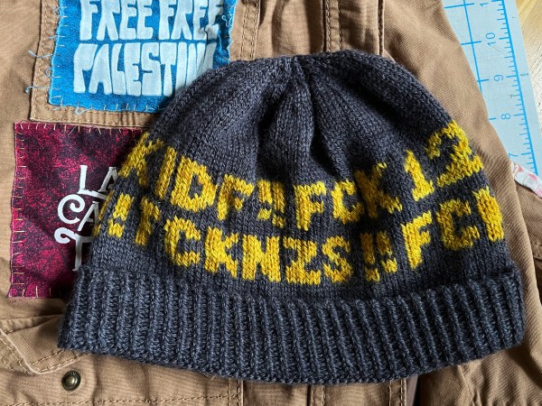 hat with words on it laying flat on top of a jacket with patches—visible words are FCK 12 and FCK NZS