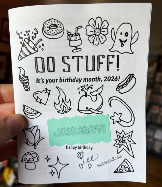 hand holding zine that says "Do Stuff! It's your birthday month, 2026!" with drawings of emojis and green sticker that says "January!"